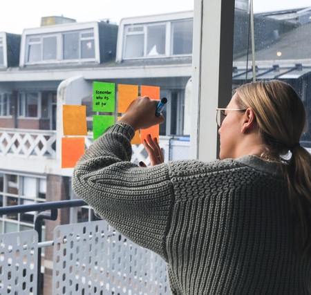 A woman writing on post-it notes stuck on the window of her apartment